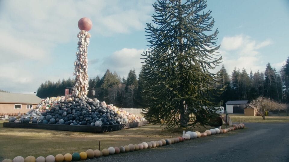 a still from a short documentary about a beachcomber in Washington, with a tall column of plastic buoys coming out of a pile on the lawn