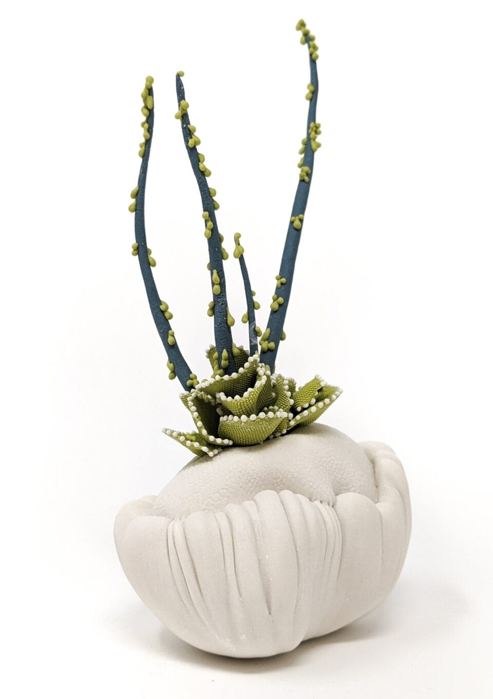 a porcelain sculpture that resembles a bundle of white textile with frills, with dark green plant-like textured spikes or fronds emerging from it