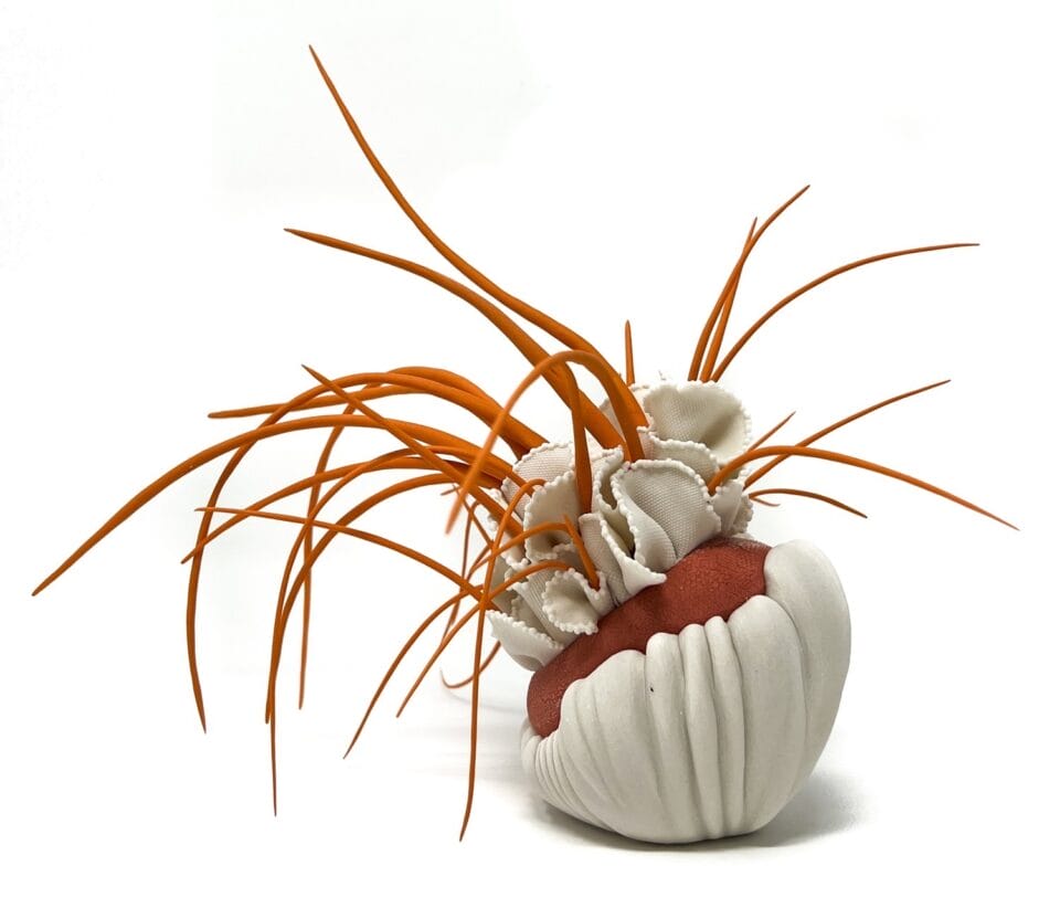 a porcelain sculpture that resembles a bundle of white-and-red textile with frills, with orange plant-like textured spikes or fronds emerging from it