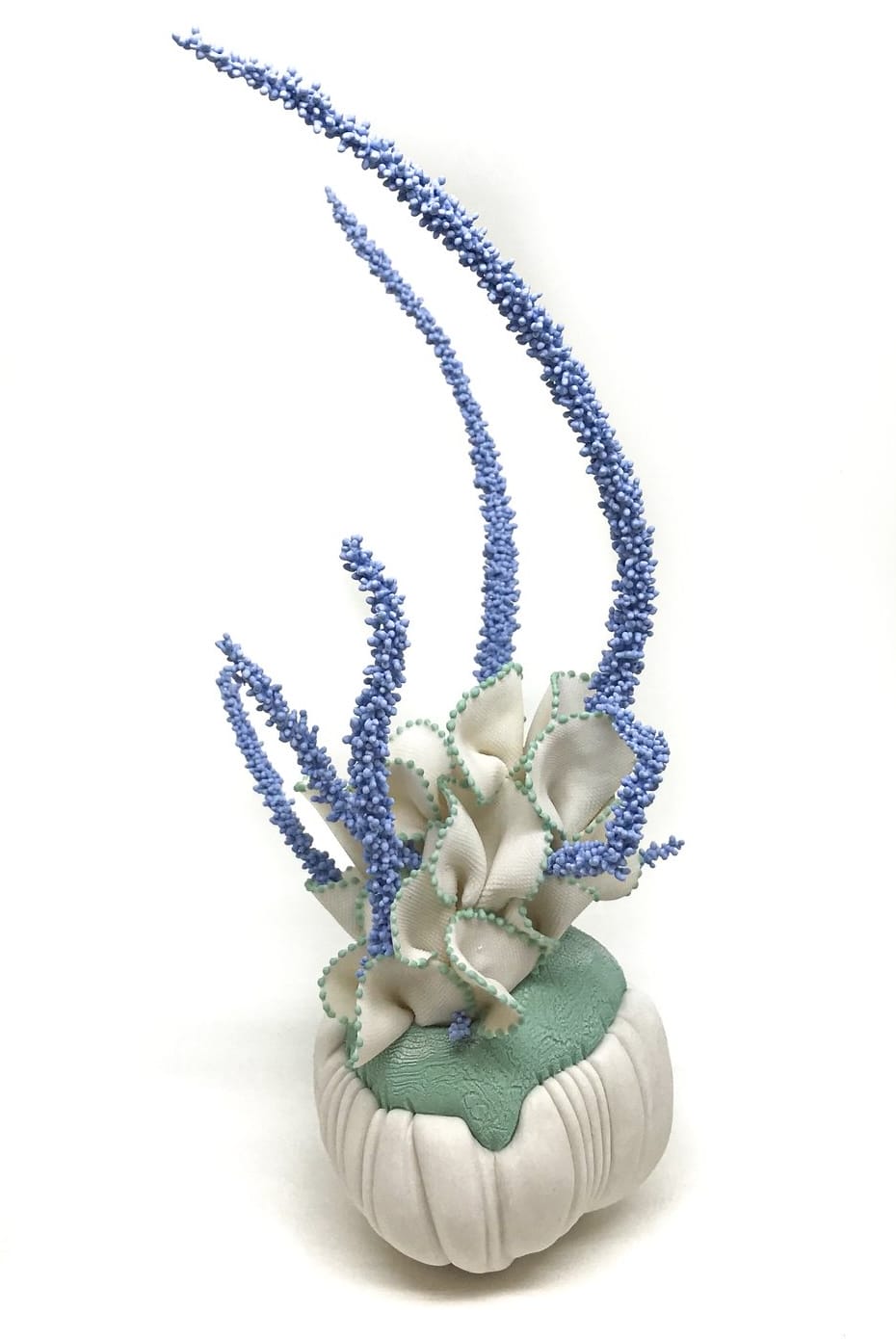 a porcelain sculpture that resembles a bundle of white-and-green textile with frills, with blue plant-like textured spikes or fronds emerging from it