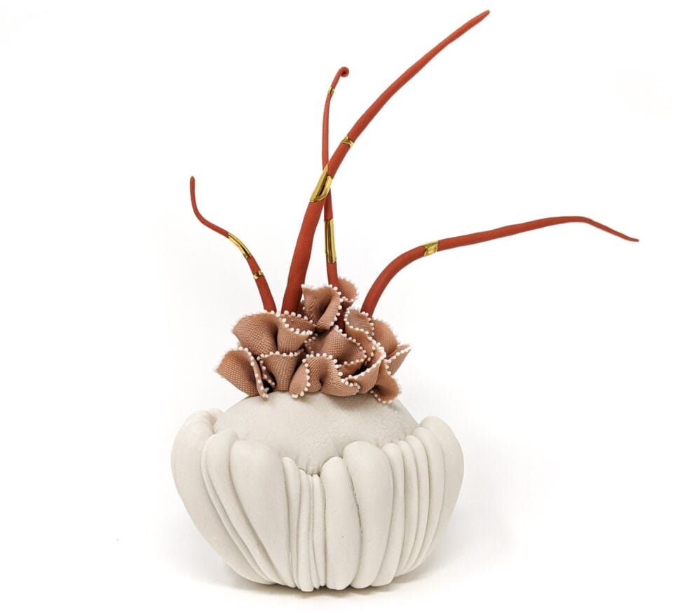 a porcelain sculpture that resembles a bundle of white textile with pink frills, with dark orange plant-like textured spikes or fronds emerging from it