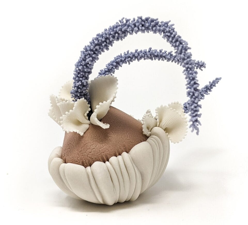 a porcelain sculpture that resembles a bundle of white-and-brown textile with frills, with blue plant-like textured spikes or fronds emerging from it