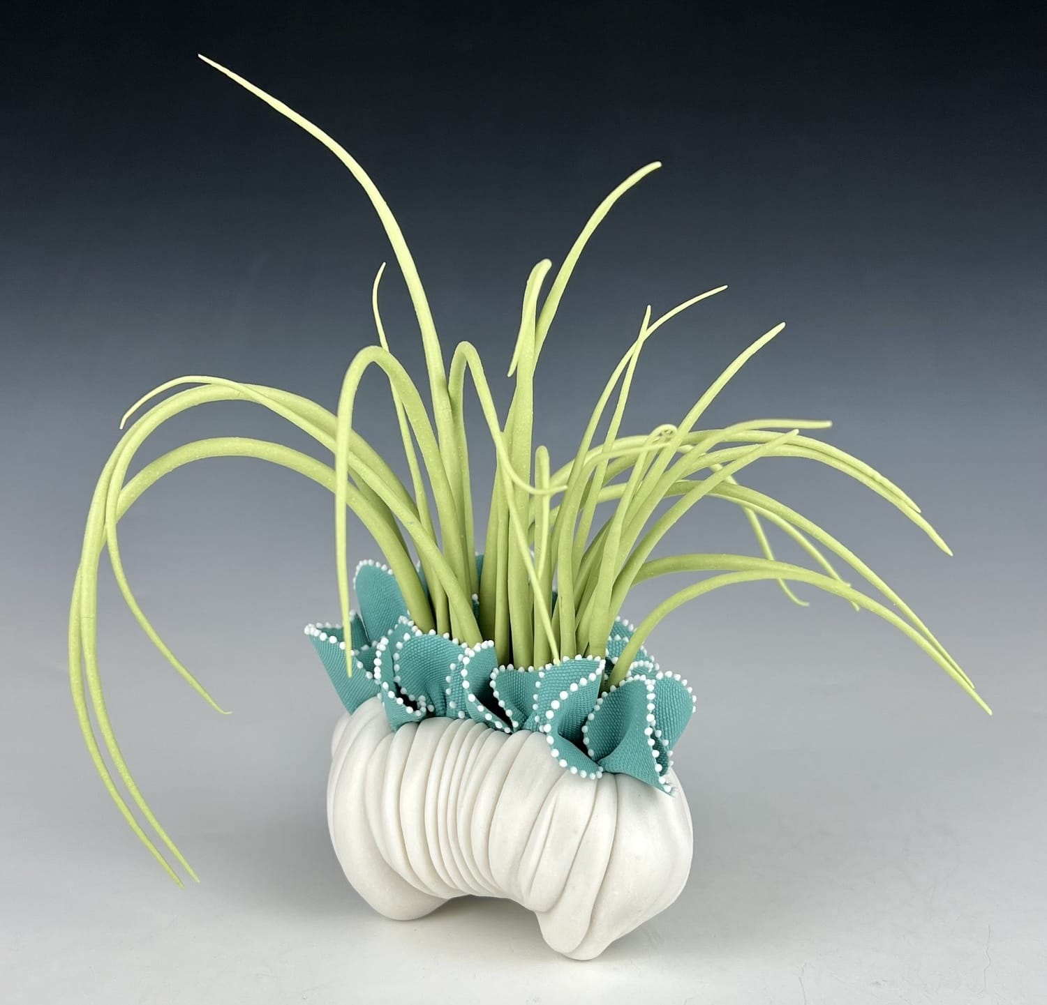 a porcelain sculpture that resembles a bundle of textile with frills, with bright green grass-like spikes or fronds emerging from it