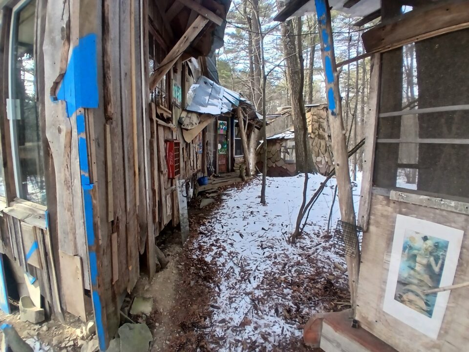 buildings in a snowy wooded landscape, part of "B-Home," a collection of intuitively built houses, sheds, and other buildings made from salvaged materials