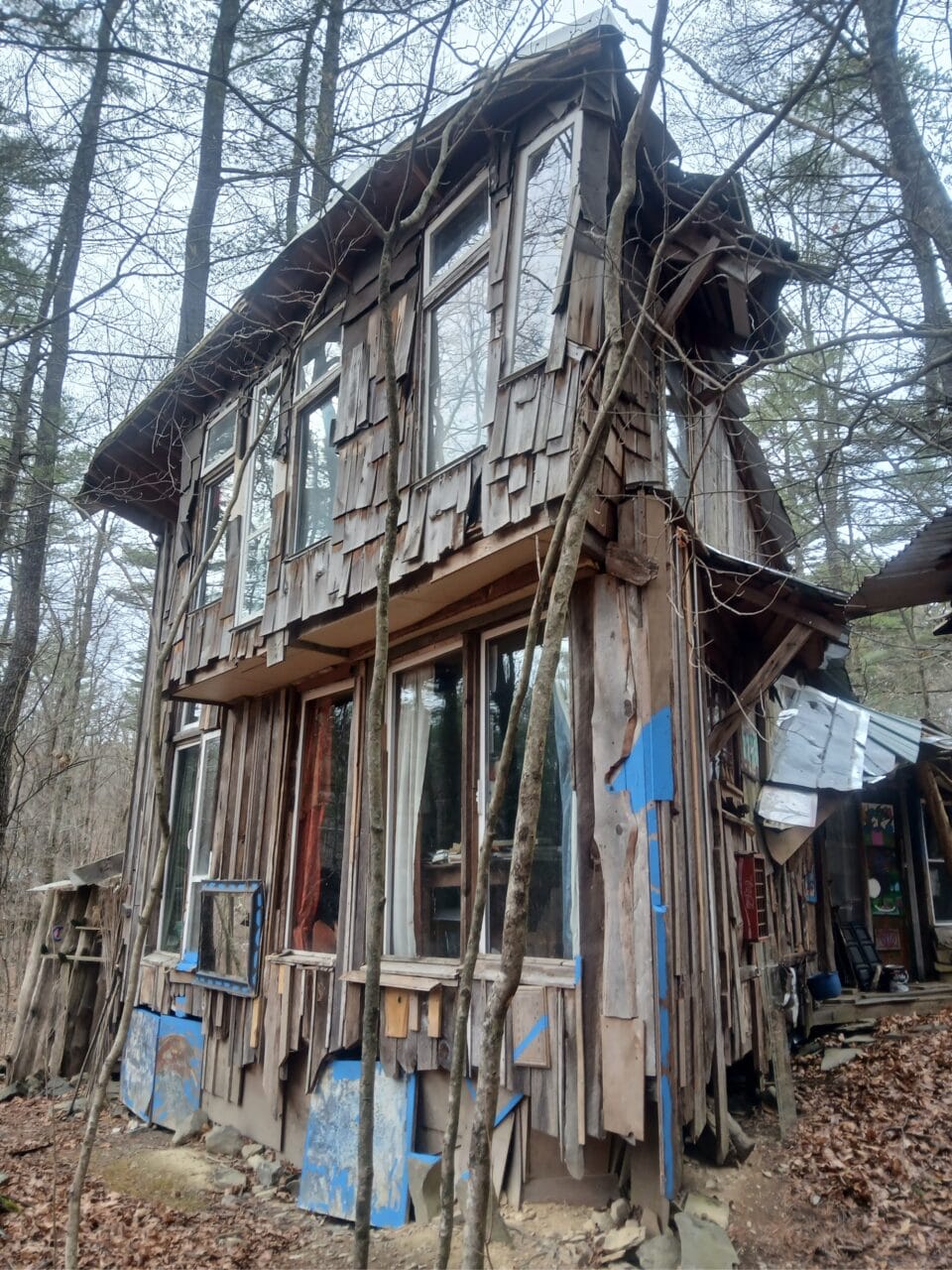 a hand-built shed-like structure in a snowy wooded landscape, part of "B-Home," a collection of intuitively built structures from salvaged materials