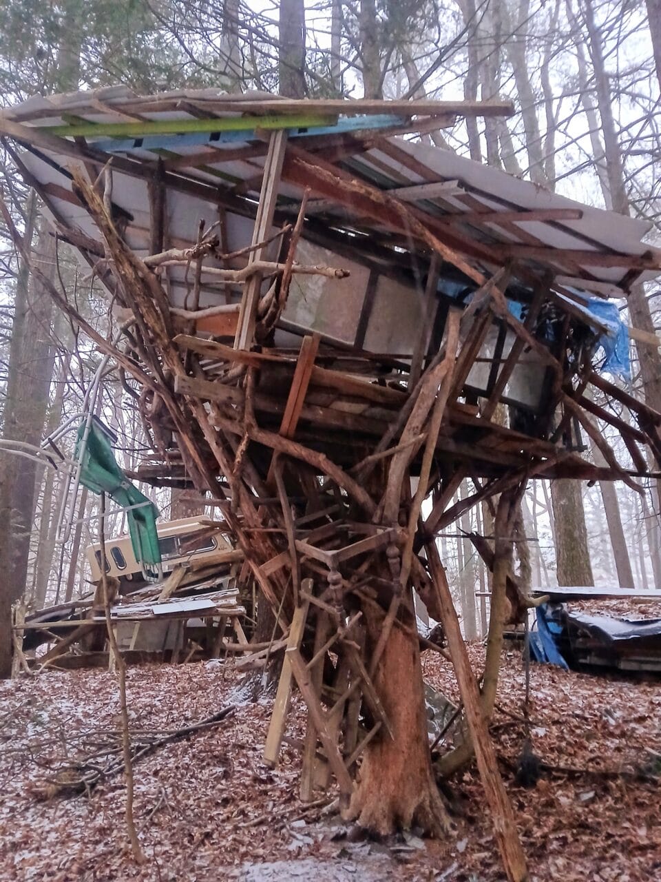 a hand-built shed-like structure in a snowy wooded landscape, part of "B-Home," a collection of intuitively built structures from salvaged materials