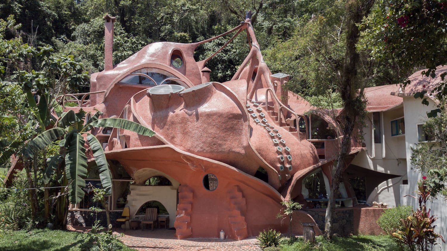 the exterior of an organically-shaped home with circular windows, circular details that resemble suckers on octopus tentacles, and varying convex slopes of terra-cotta tones