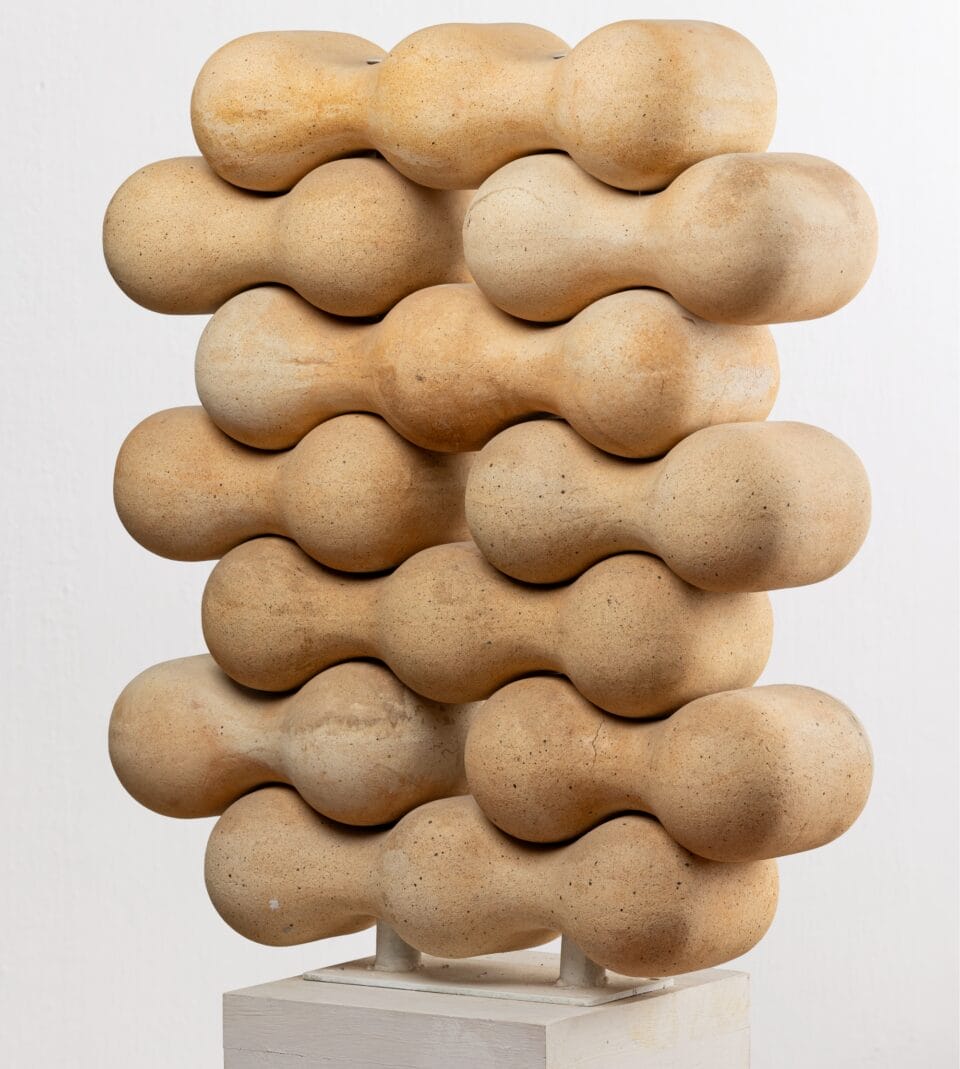 a vertical sculpture of peanut-shaped forms slotted together on a white pedestal