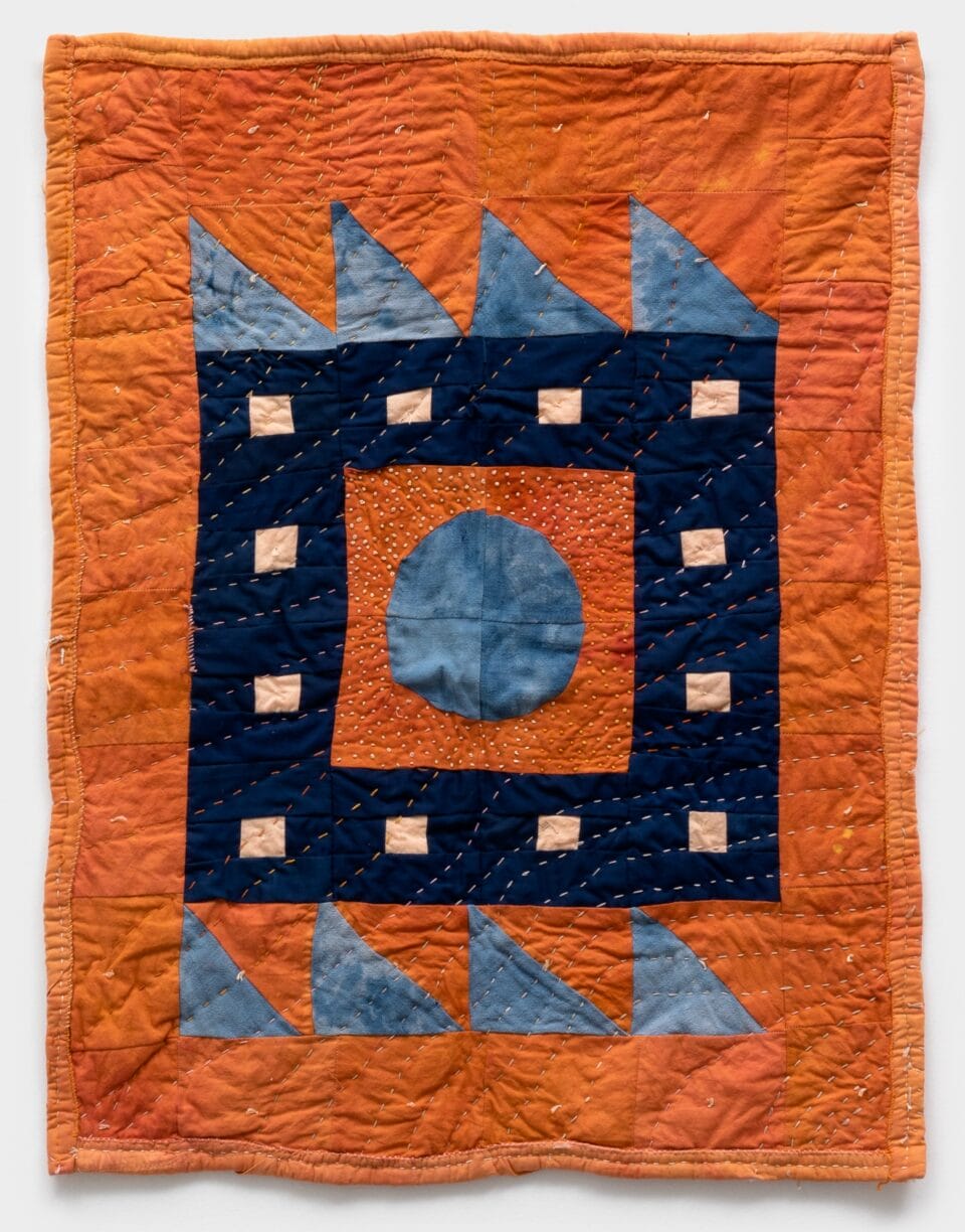 a vertical quilted geometric composition made with naturally dyed fabrics, primarily in bright orange, light blue, dark blue, and peach