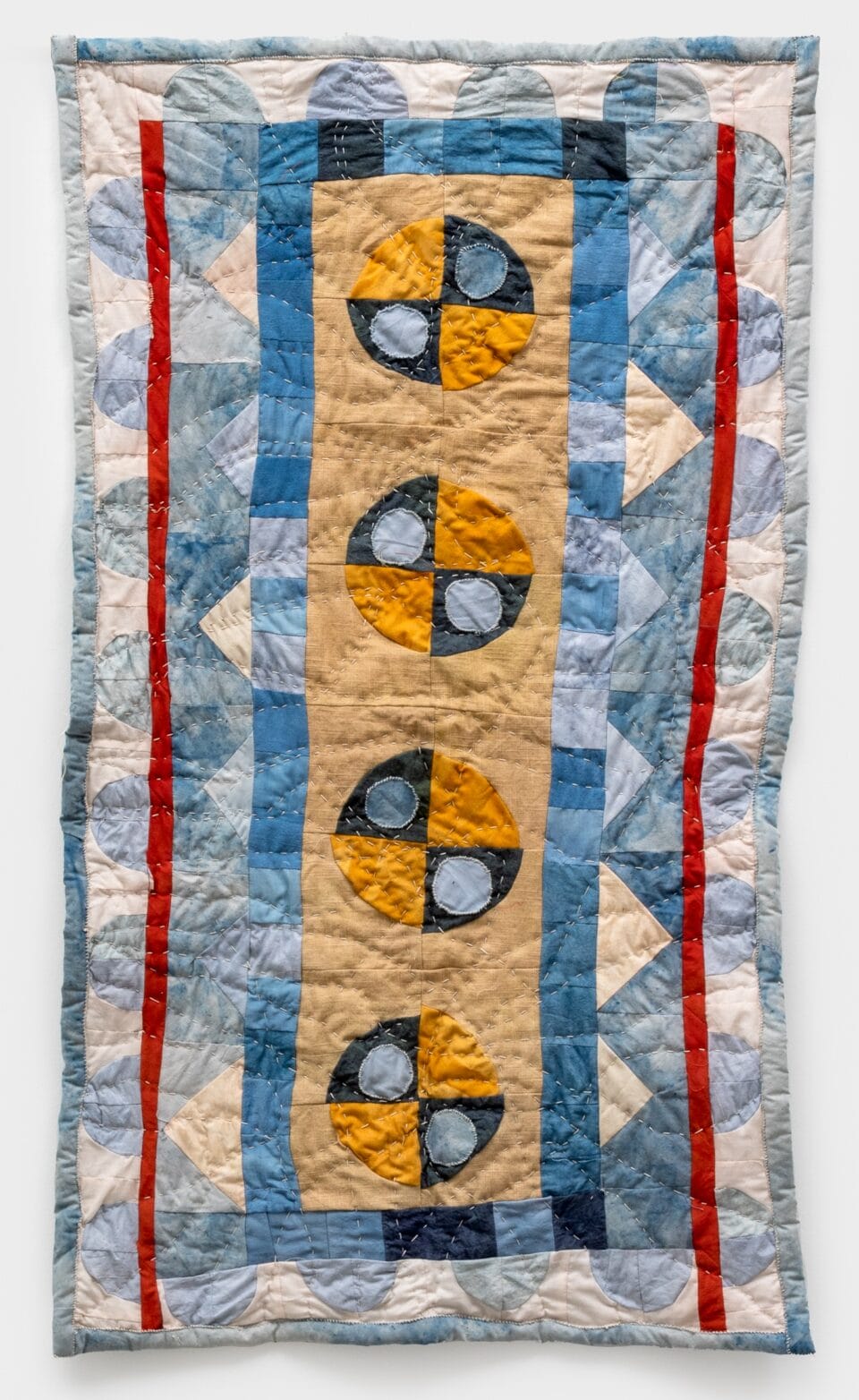 a vertical quilted geometric composition made with naturally dyed fabrics, primarily in yellow, blue, white, and red