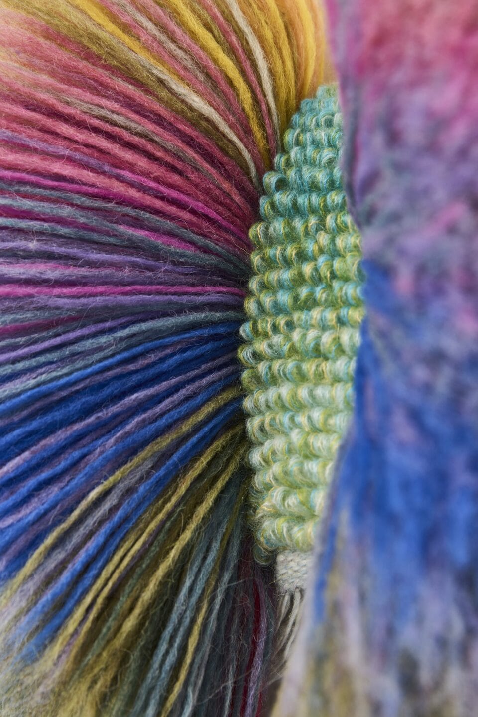 a detail of an abstract, vibrantly colored weaving with green in the center and radiating fiber in other colors