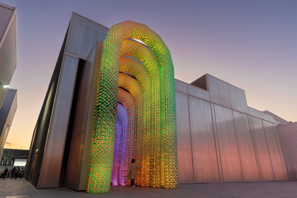 a monumental illuminated archway installed at the entrance of a contemporary building with a vibrant geometric gradient pattern