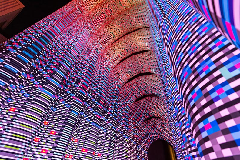 a detail looking skyward of a monumental illuminated archway installation with a pink-and-purple geometric pattern