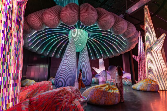 people stands beneath an illuminated installation with lights resembling the underside of a mushroom