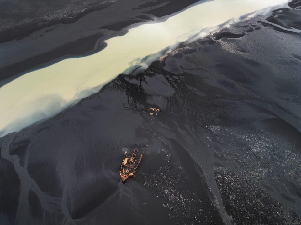 an aerial photo of a broken wooden boat floating in dark waters