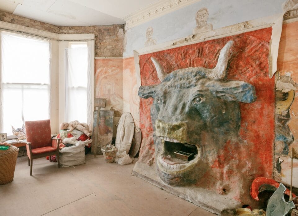 the interior of Ron Gittins' apartment in Birkenhead, England, featuring a very ornate, hand-sculpted fireplace of a bull's head with murals all around on the walls