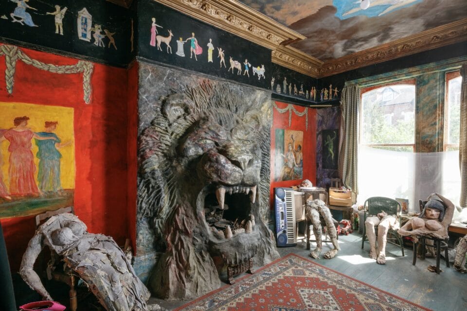 the interior of Ron Gittins' apartment in Birkenhead, England, featuring a very ornate, hand-sculpted fireplace of a lion's head with murals all around on the walls