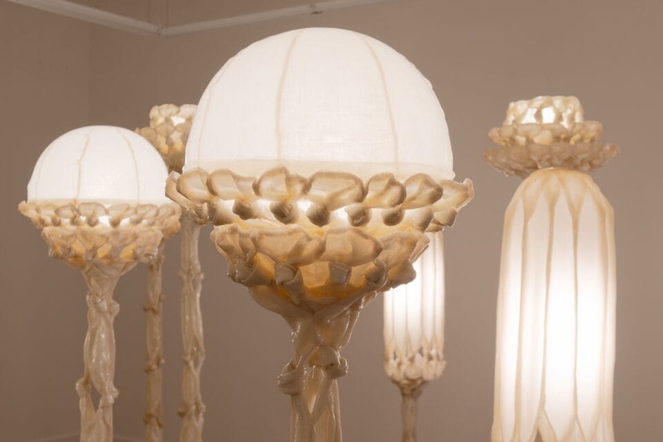 details of the tops of a number of sculptural white lamps made from pieces of fabric coated in bio resin and knotted, illuminated and displayed in a white gallery space