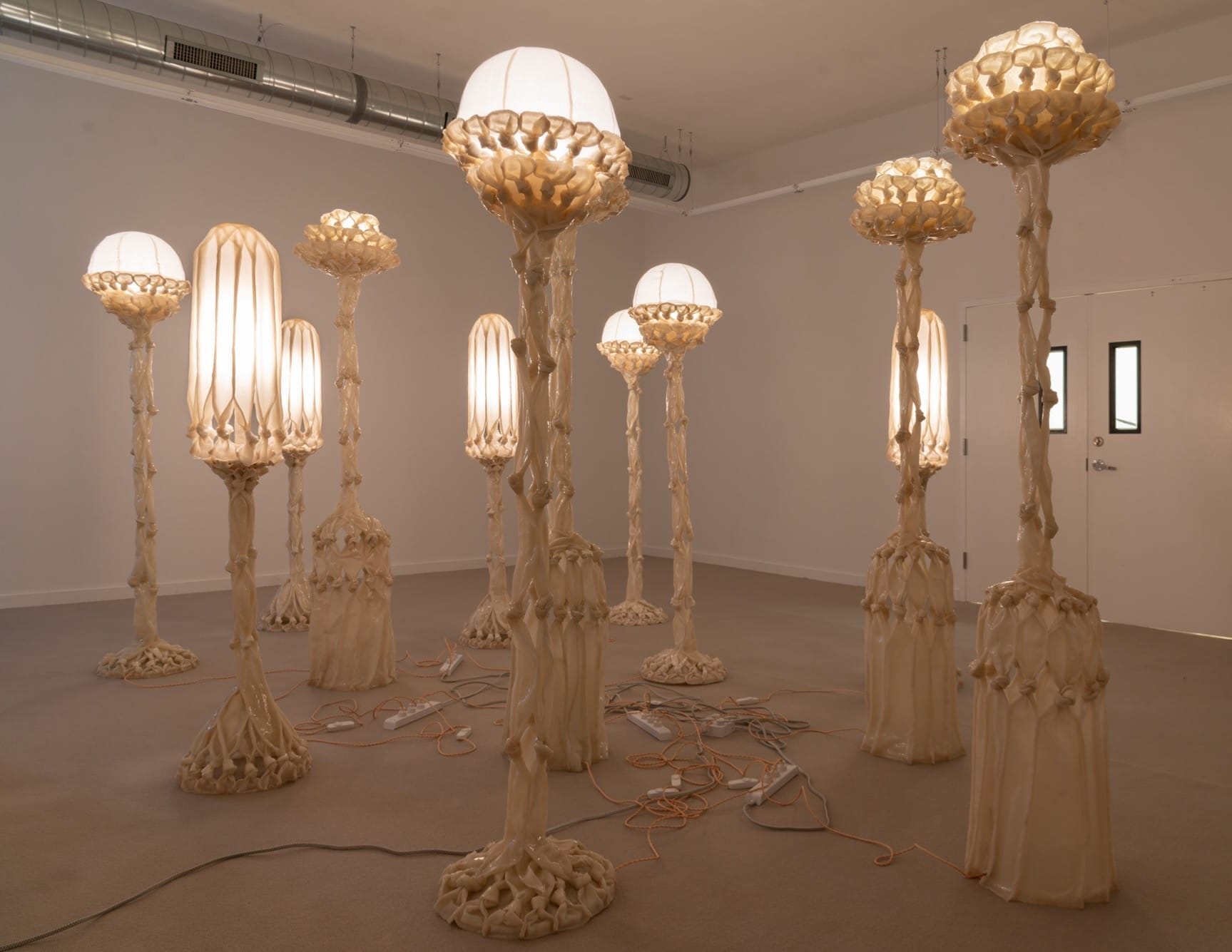 a group of sculptural white lamps made from pieces of fabric coated in bio resin and knotted, illuminated and displayed in a white gallery space