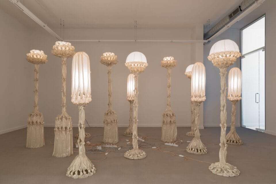 a group of sculptural white lamps made from pieces of fabric coated in bio resin and knotted, displayed in a white gallery space