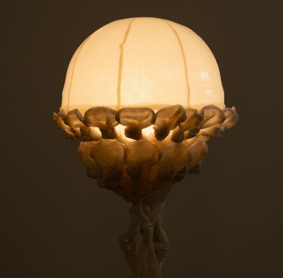 the top of a sculptural lamp, illuminated in the dark, made from twisted pieces of fabric coated in bio resin and knotted