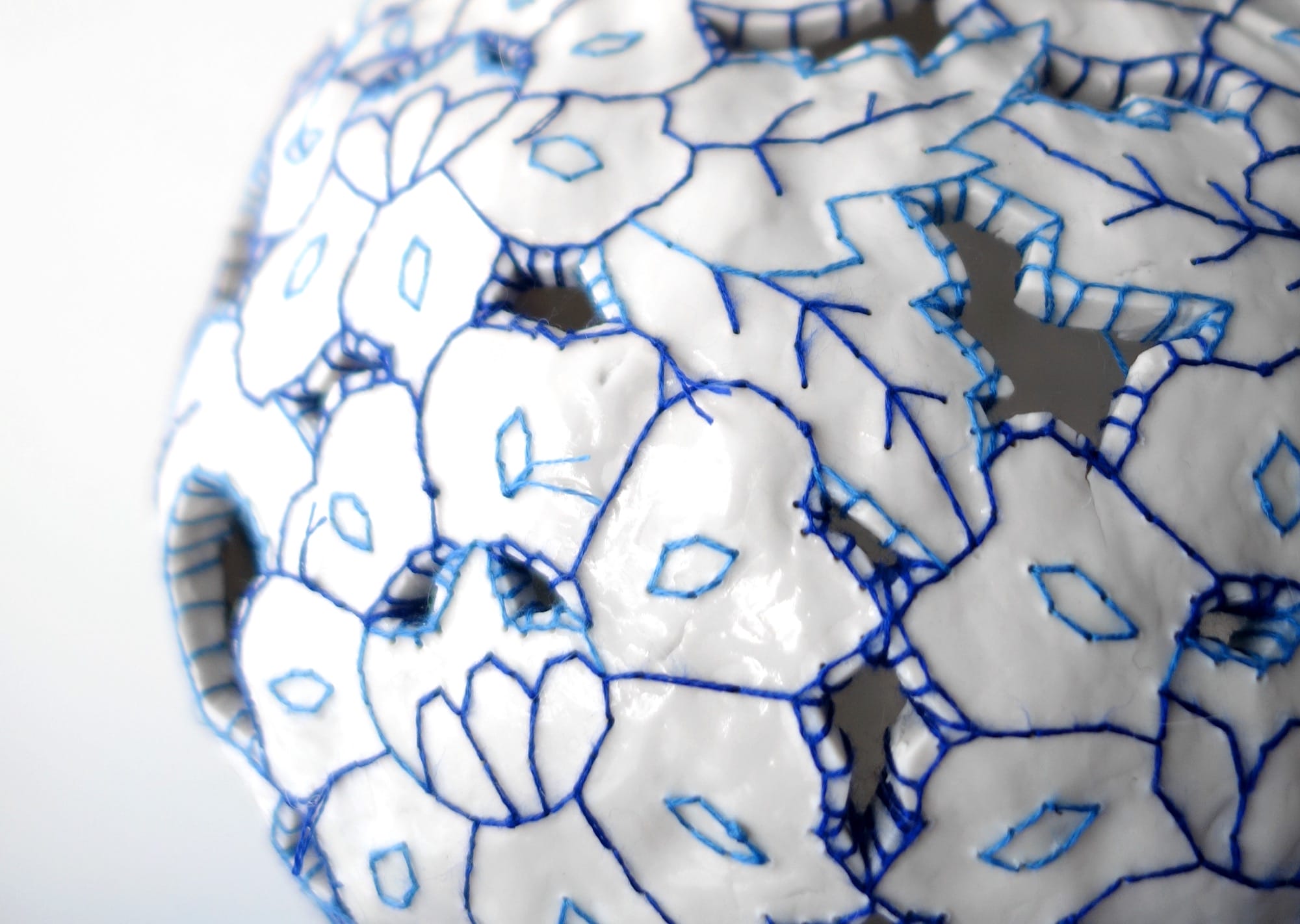 a detail of a white porcelain vessel embroidered with blue cotton thread