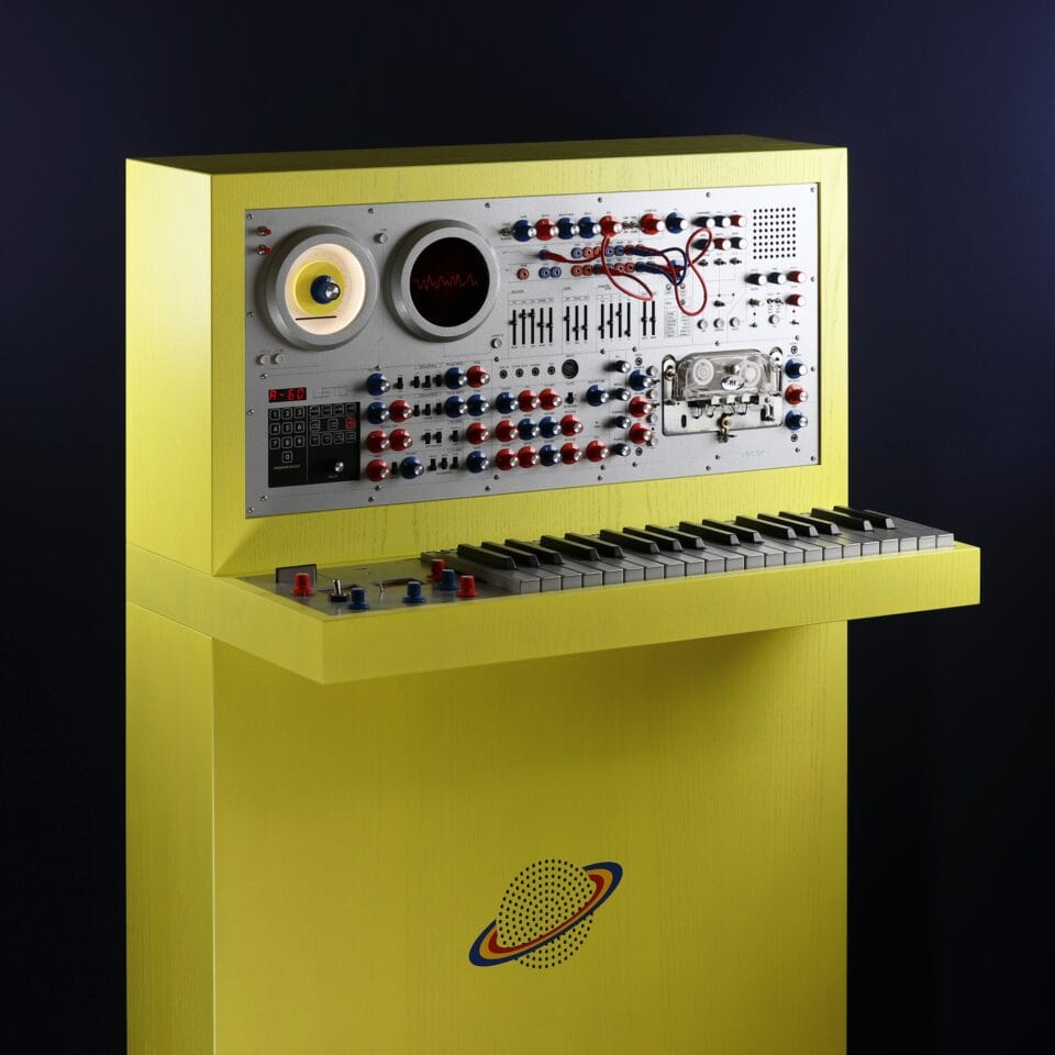 a sculpture resembling a retro computer or console in a bright yellow hue with a silver backing for numerous black buttons and dials