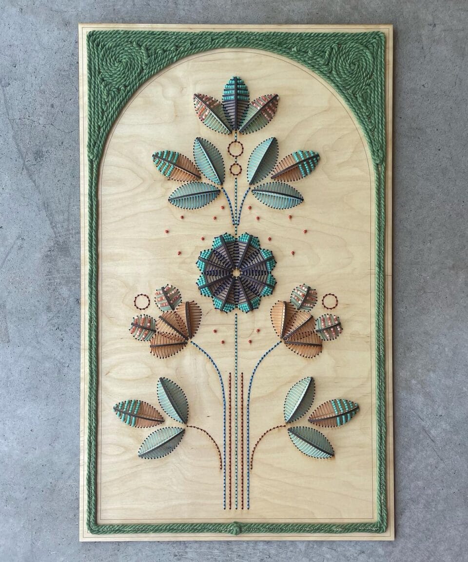 a floral embroidery in greens and blues on a wooden panel