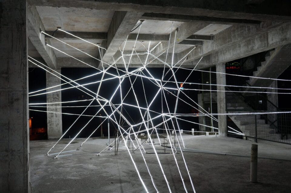 a monumental public art installation of a star shape made from LED strips inside of a concrete and steel building at night