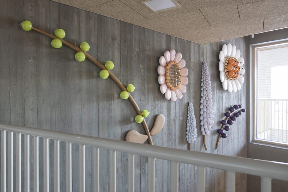 an installation of botanical sculptures mounted on the wall of a stairwell made from glass, wood, and ceramics