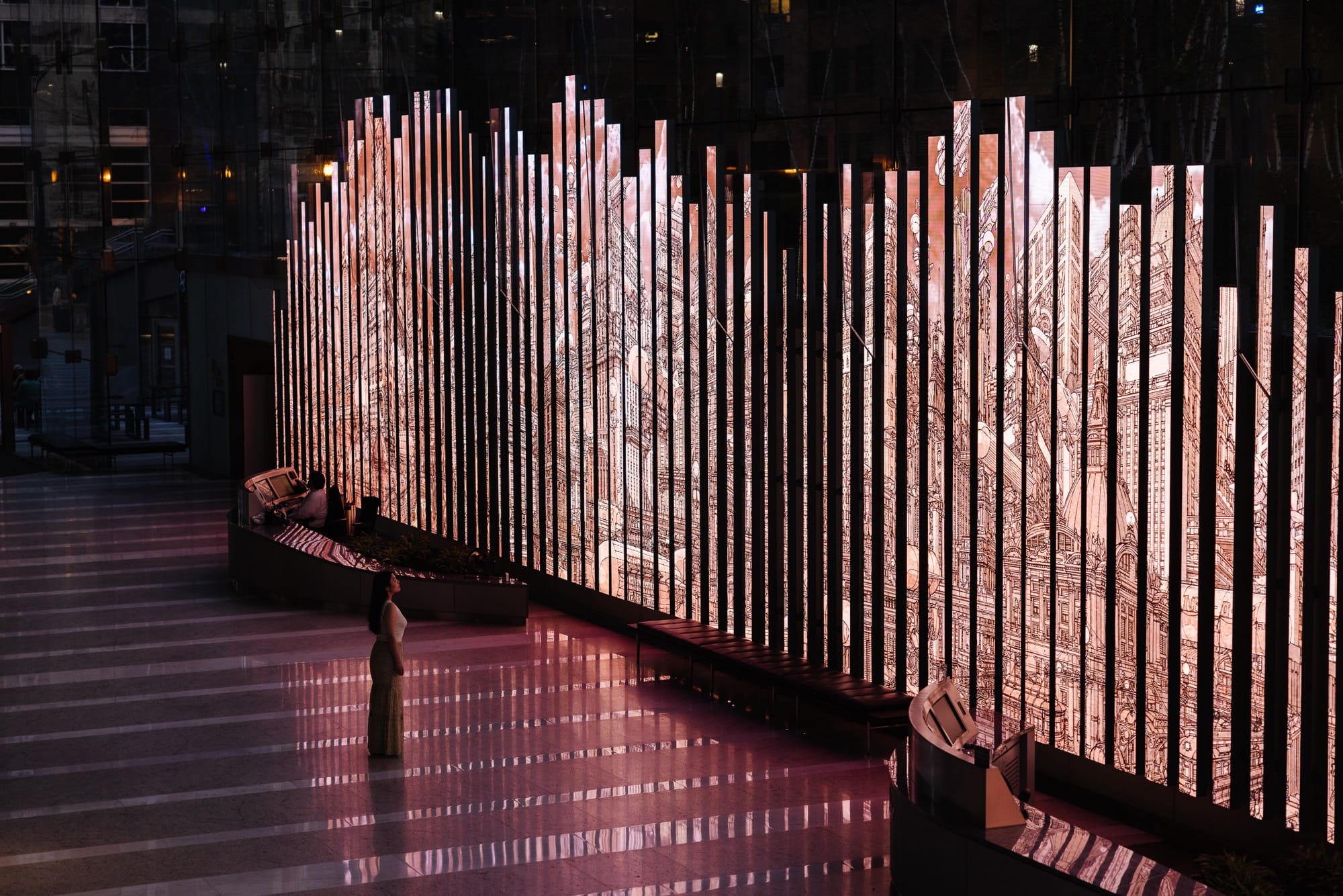 a person stands in front of an illuminated installation with architectural drawings