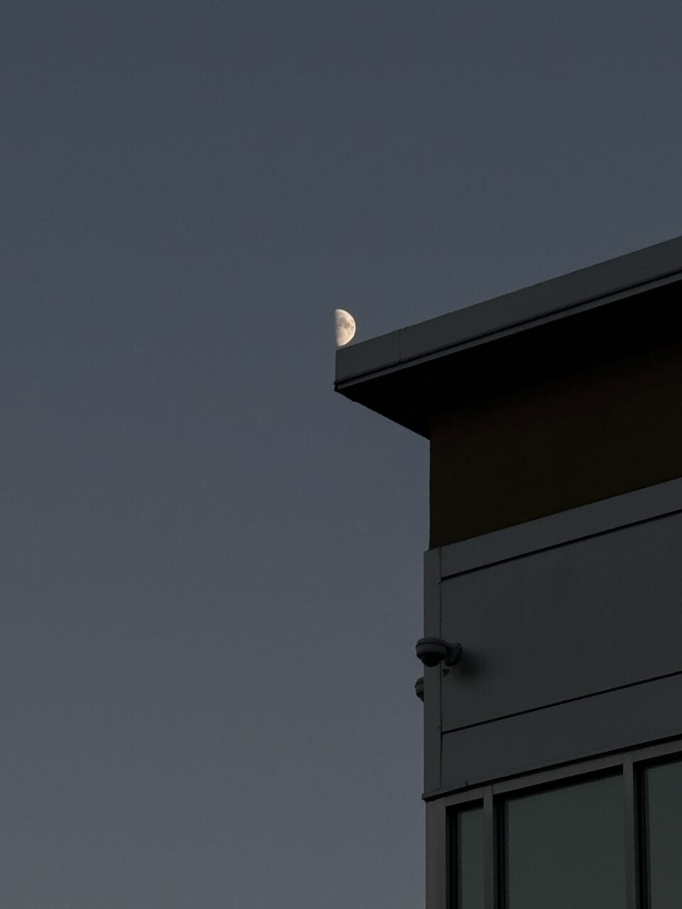 a photograph of a corner of a building at night, with the moon perched on the tip of it