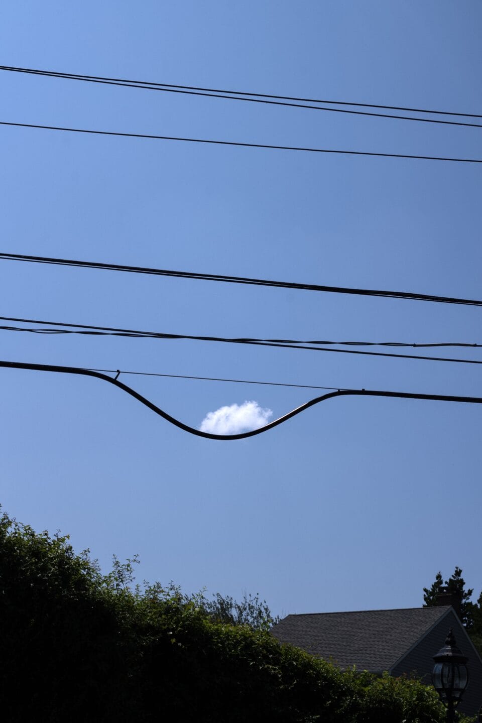 a photograph of electrical wires that appear to be cradling a single white cloud in a blue sky