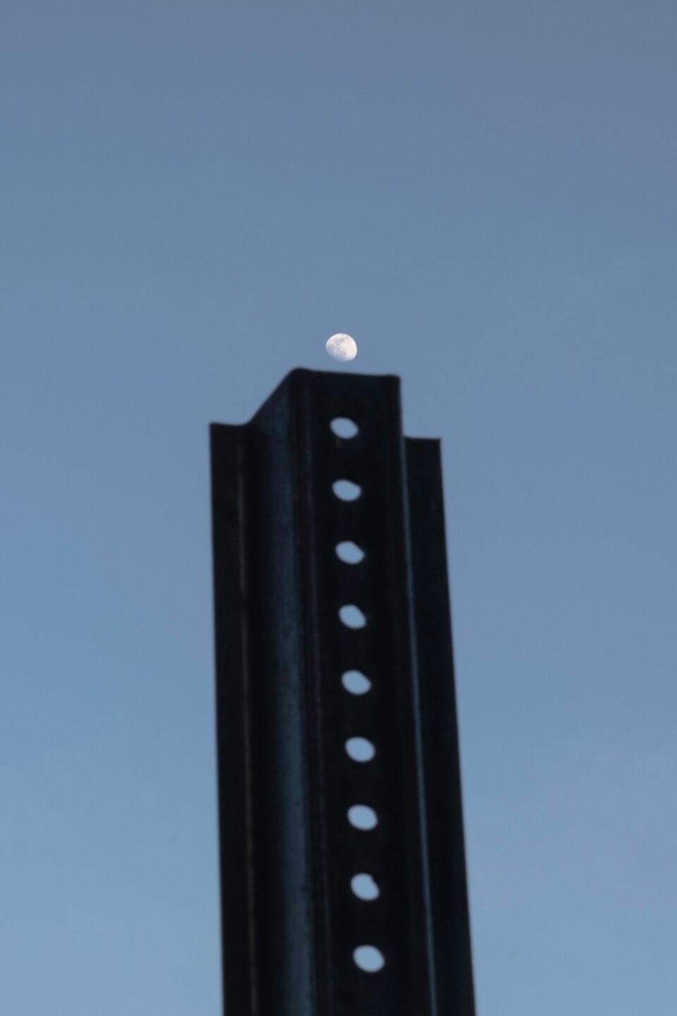 a vertical photograph of a tall building with a stack of round windows, photographed at dusk with the moon hovering just above the building as if it's another window