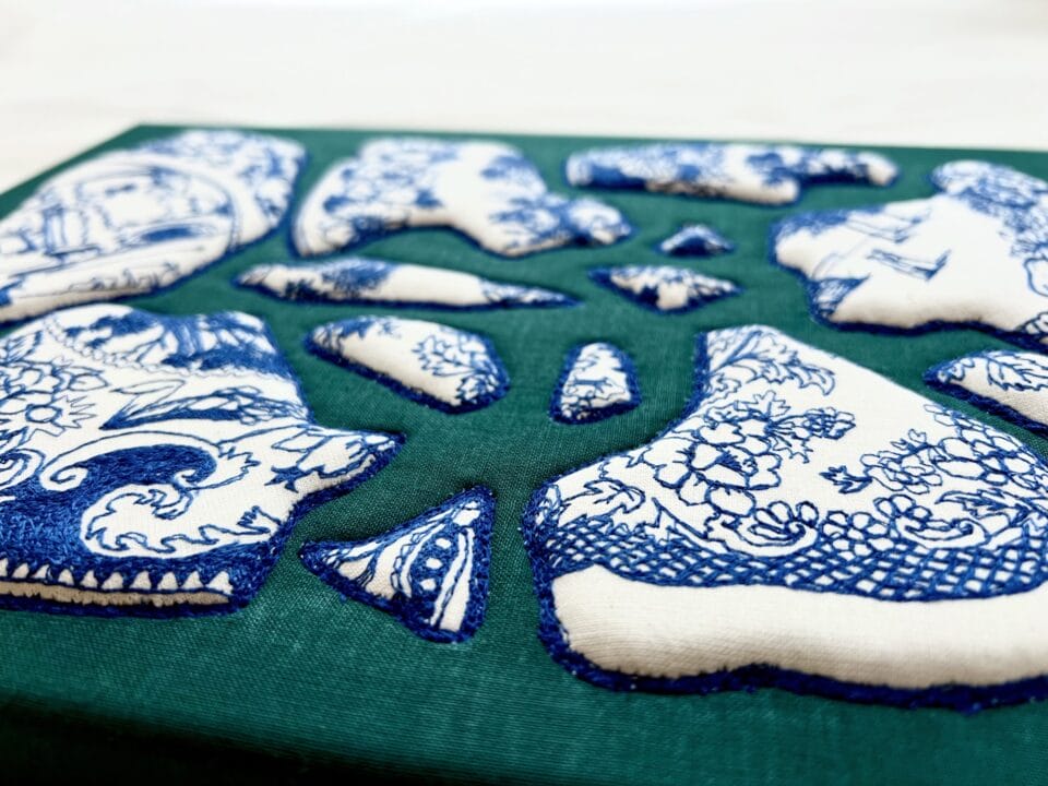 a detail of a textile artwork of blue-and-white porcelain plate pieces appliqued on a green background