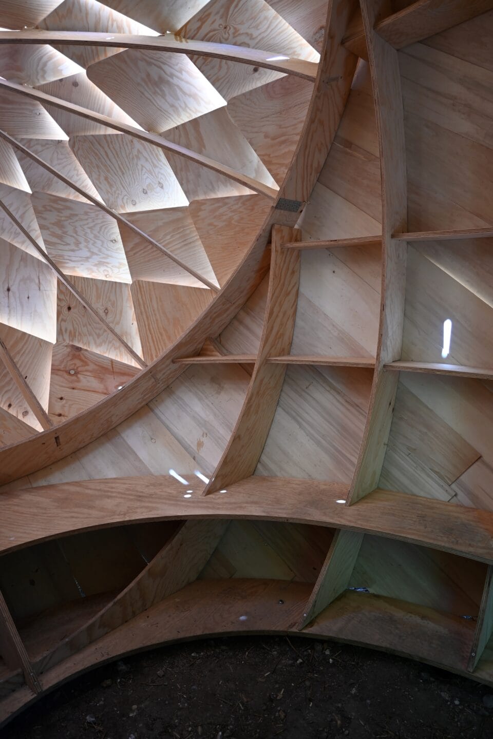 the inside of a wooden structure. a bench encircles the base and sun streams through layered diamond shapes on the wall