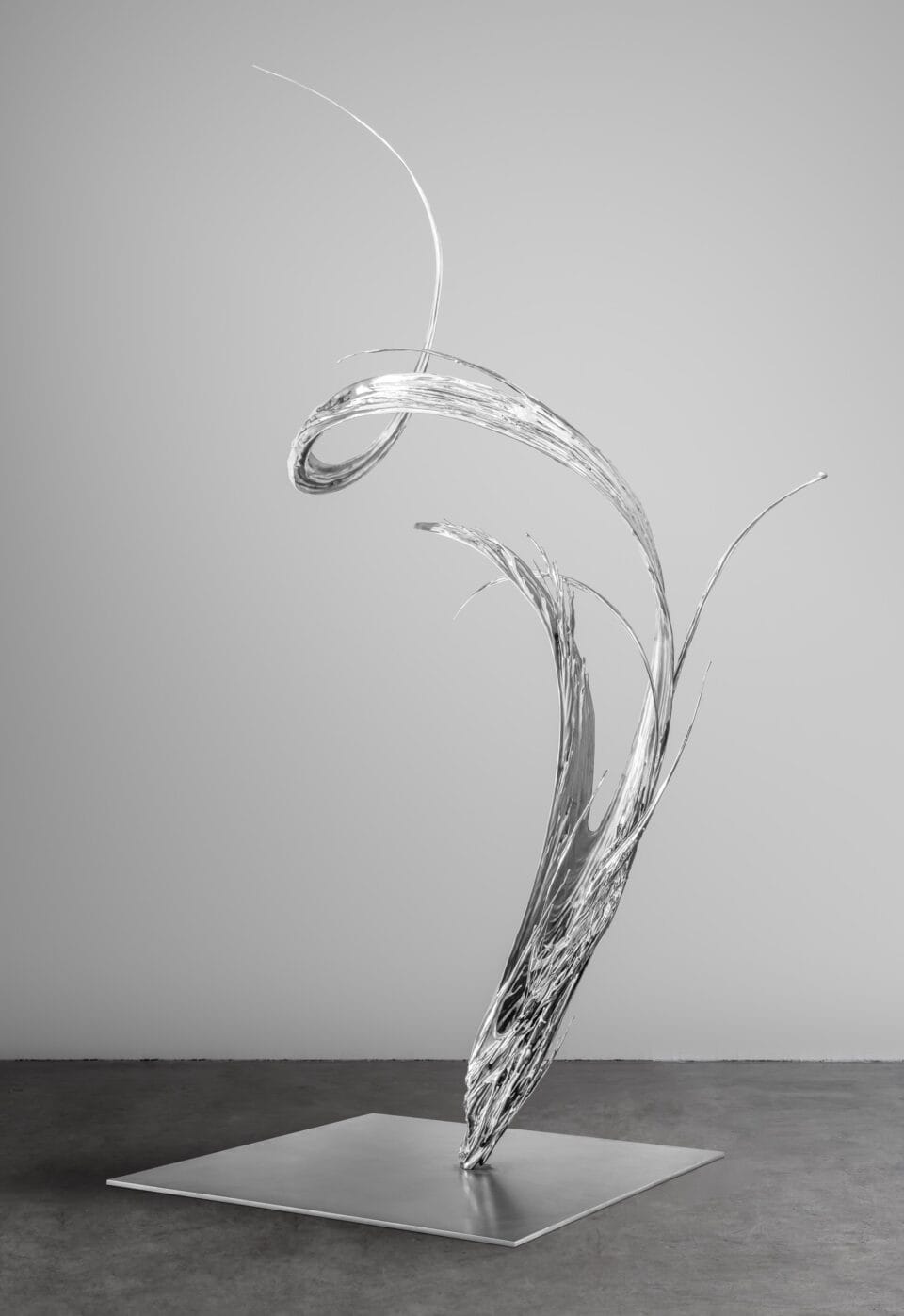 a chrome-colored sculpture on a metal base in an abstract form of swirling liquid