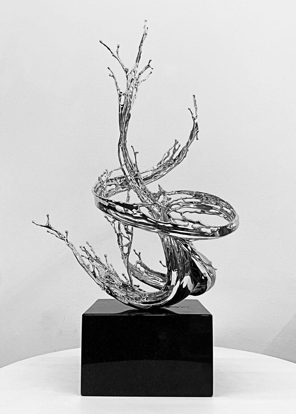 a chrome-colored sculpture on a black pedestal in an abstract form of swirling liquid