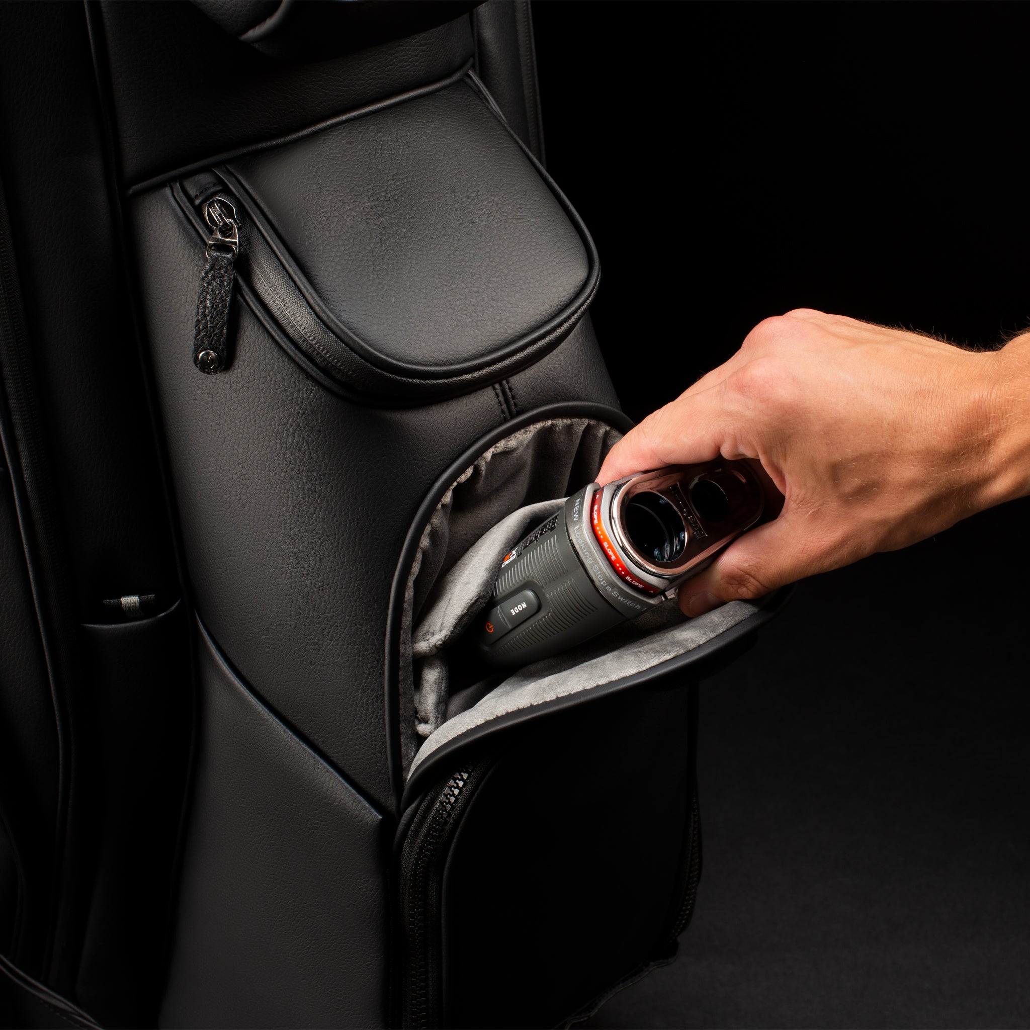 Range finder being put into black leather golf cart bag