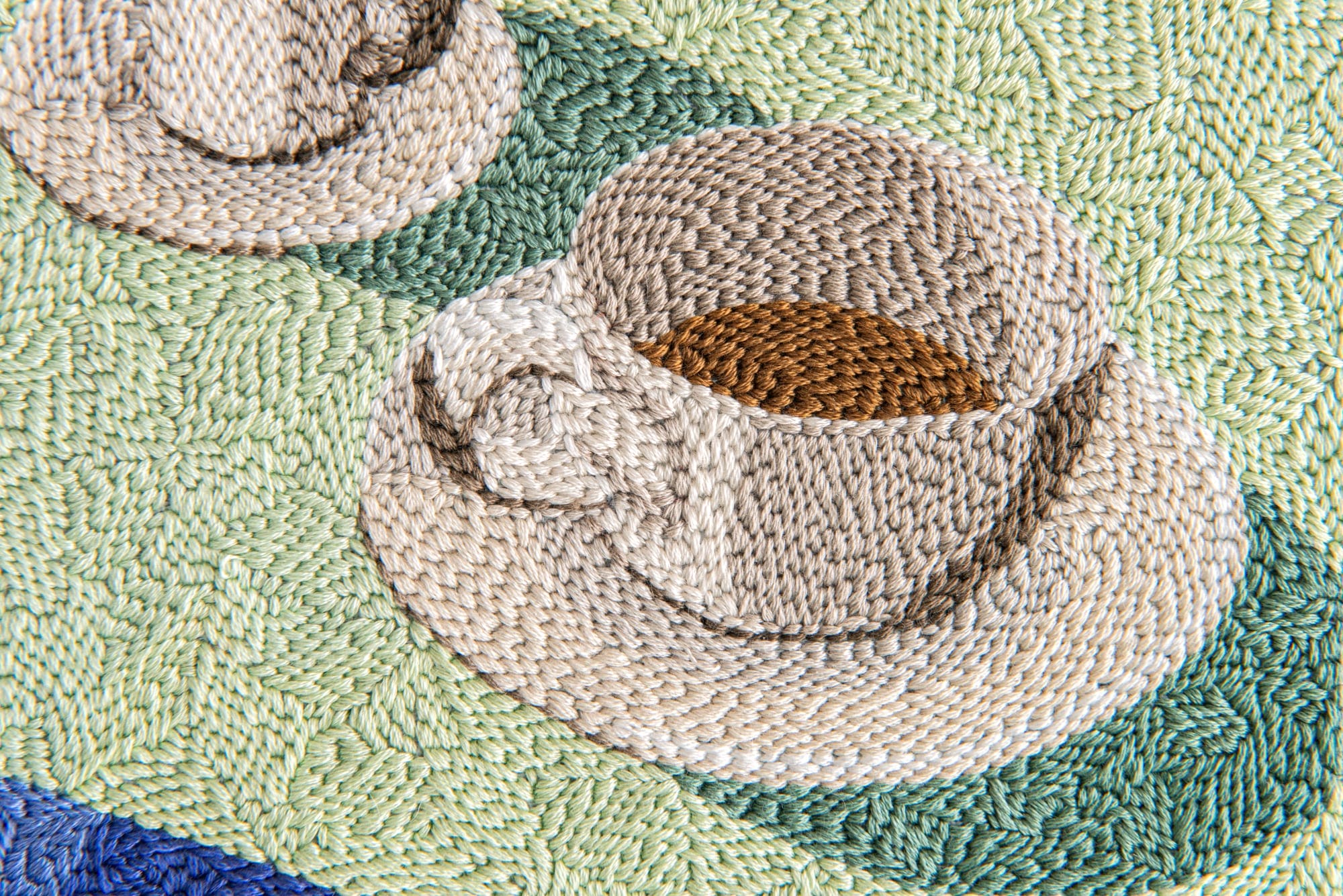 a detail image of an embroidery of two coffee cups on an outdoor table with a blue bottle nearby