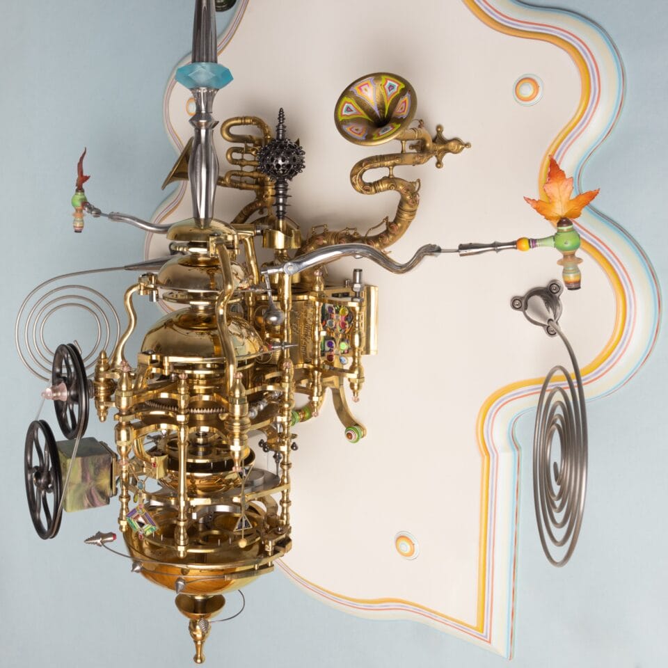 a detail of the lower part of an elaborately detailed sculpture with a clockwork mechanism and numerous sculpted and painted elements installed on an ornately shaped white panel, with some of the elements able to be moved and rotated to show different scenes