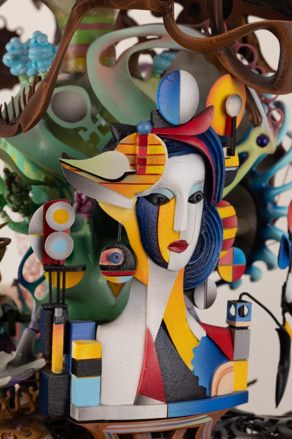 a close-up detail of part of an elaborately decorated sculpture with numerous sculpted, found, and painted elements, emphasizing a woman's face in the style of modern painters like Delaunay or Mondrian