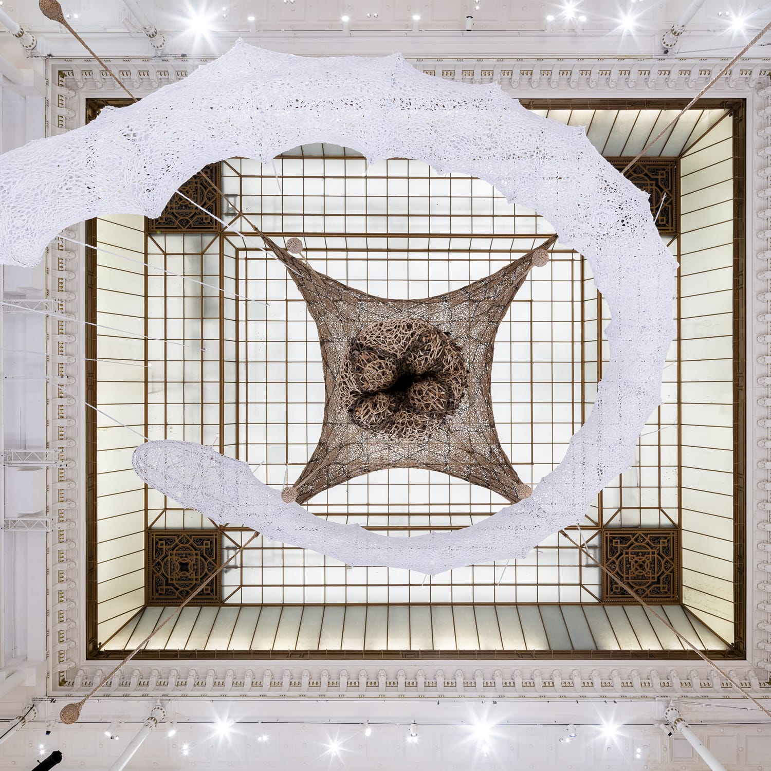 a view looking up at the atrium of a white snake net swirling upward and a square brown net hanging over