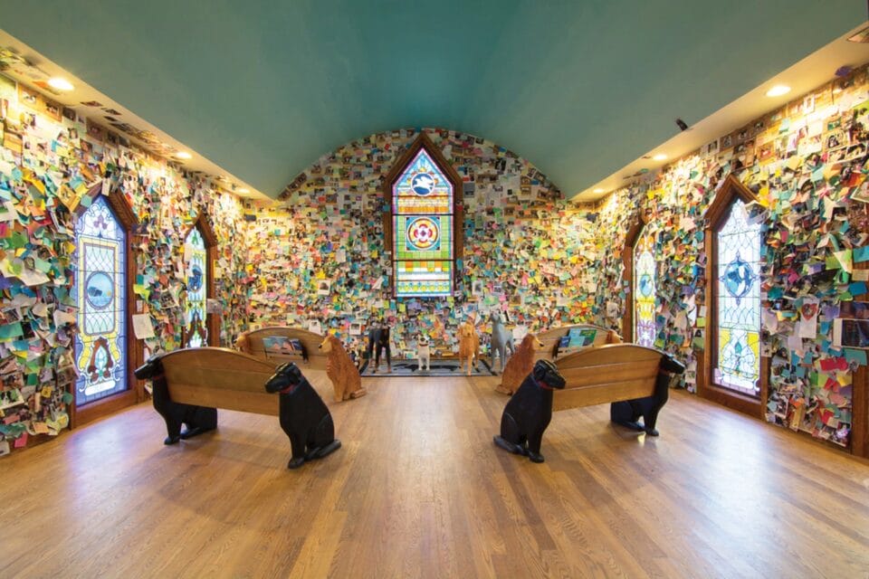 an art environment interior with pews facing a stained window and the walls coated in papers and drawings