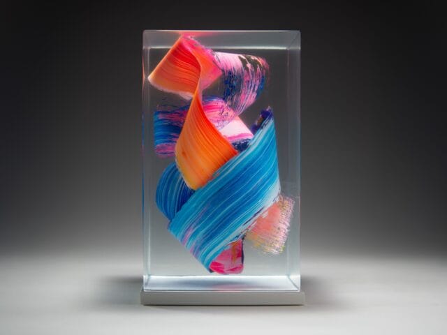 a sculpture made from cast clear resin in a cube form with three-dimensional multicolored brushstrokes inside, set against a black background