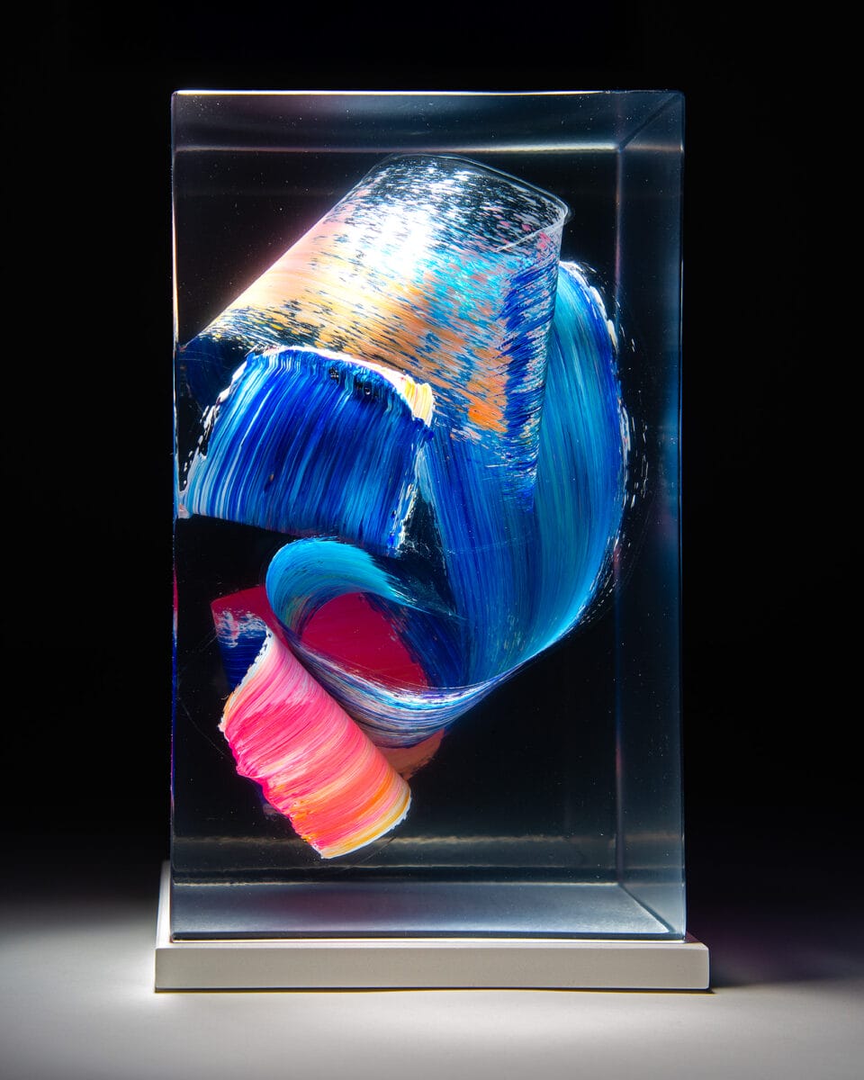 a sculpture made from cast clear resin in a cube form with three-dimensional multicolored brushstrokes inside, set against a black background