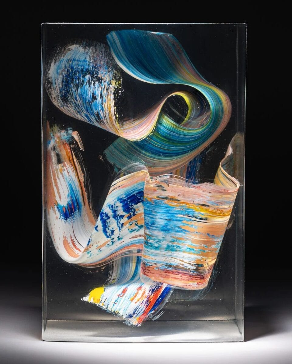 a sculpture made from cast clear resin in a cube form with three-dimensional multicolored brushstrokes inside, set against a black background