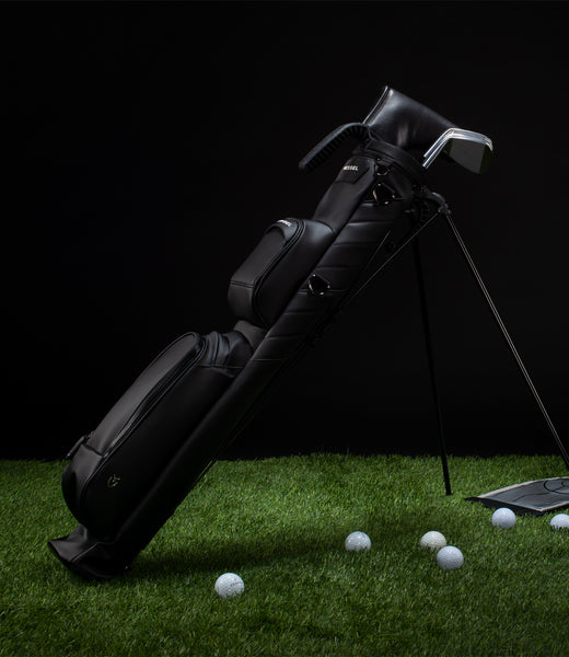 Black pencil stand bag on green grass with golf balls scattered