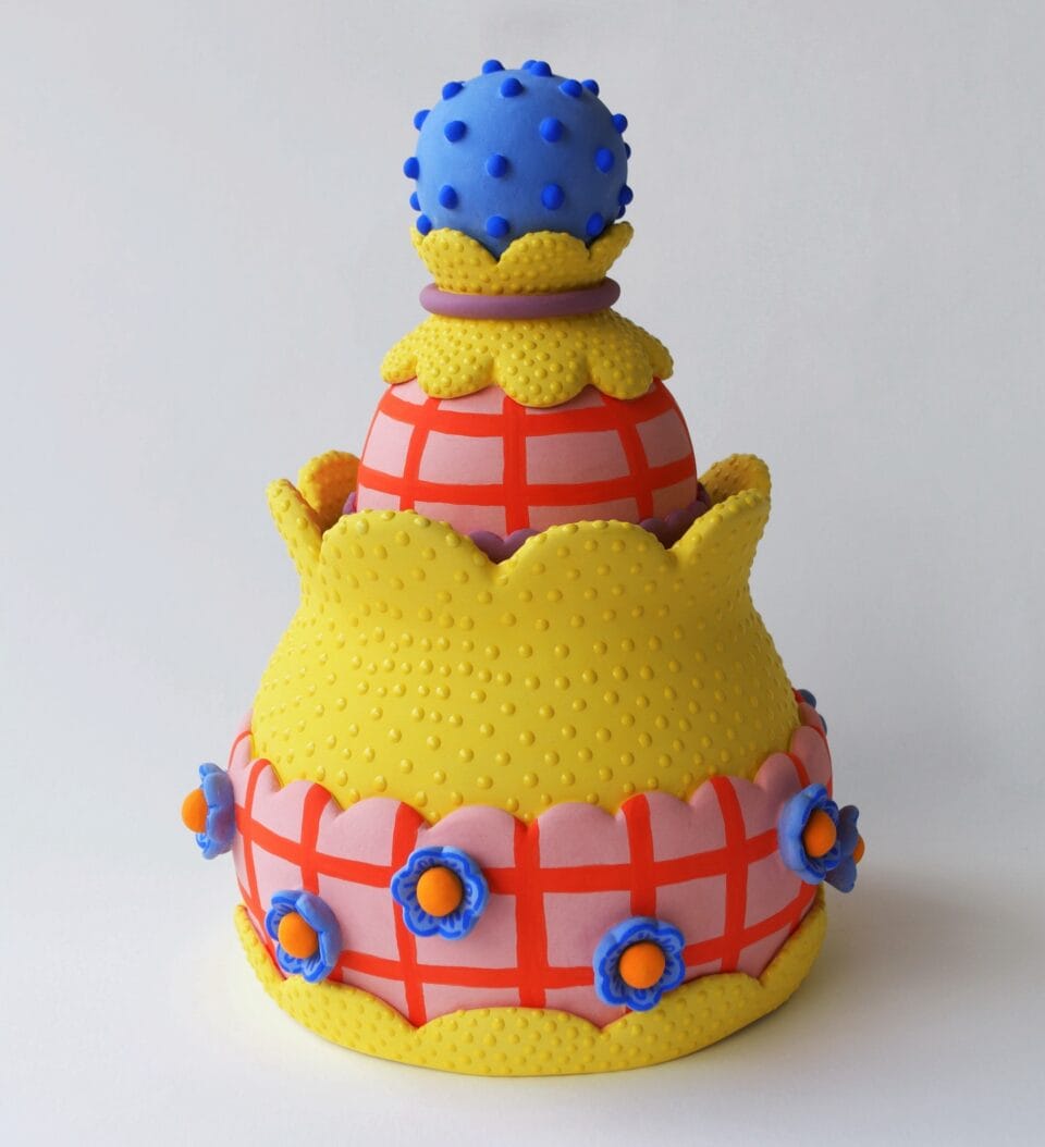 a confectionery-inspired ceramic vessel with a bright yellow body and pink plaid detail with blue flower-like bobbles