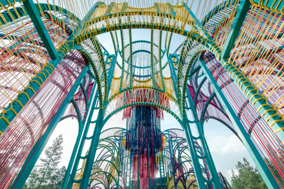 a detail of a vibrantly colored architectural pavilion made of metal poles and rope